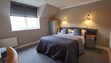A bedroom with a bed, bedside tables, a wardrobe, a radiator, a window with blinds, and a chair.