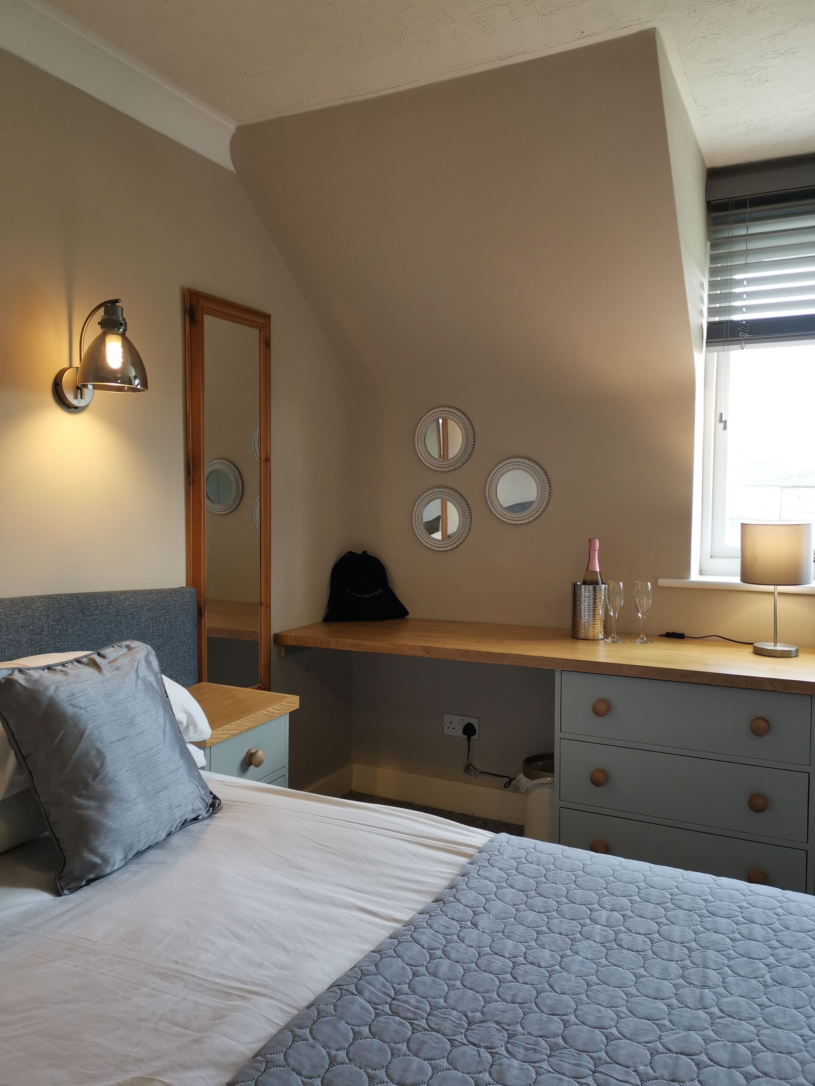 A bedroom with a bed, a dresser, a mirror, and a window.