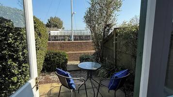 A patio area with a table and two chairs, a brick wall, and a metal fence.