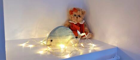 A teddy bear with a bow and a red bow tie sitting on a white shelf with string lights.