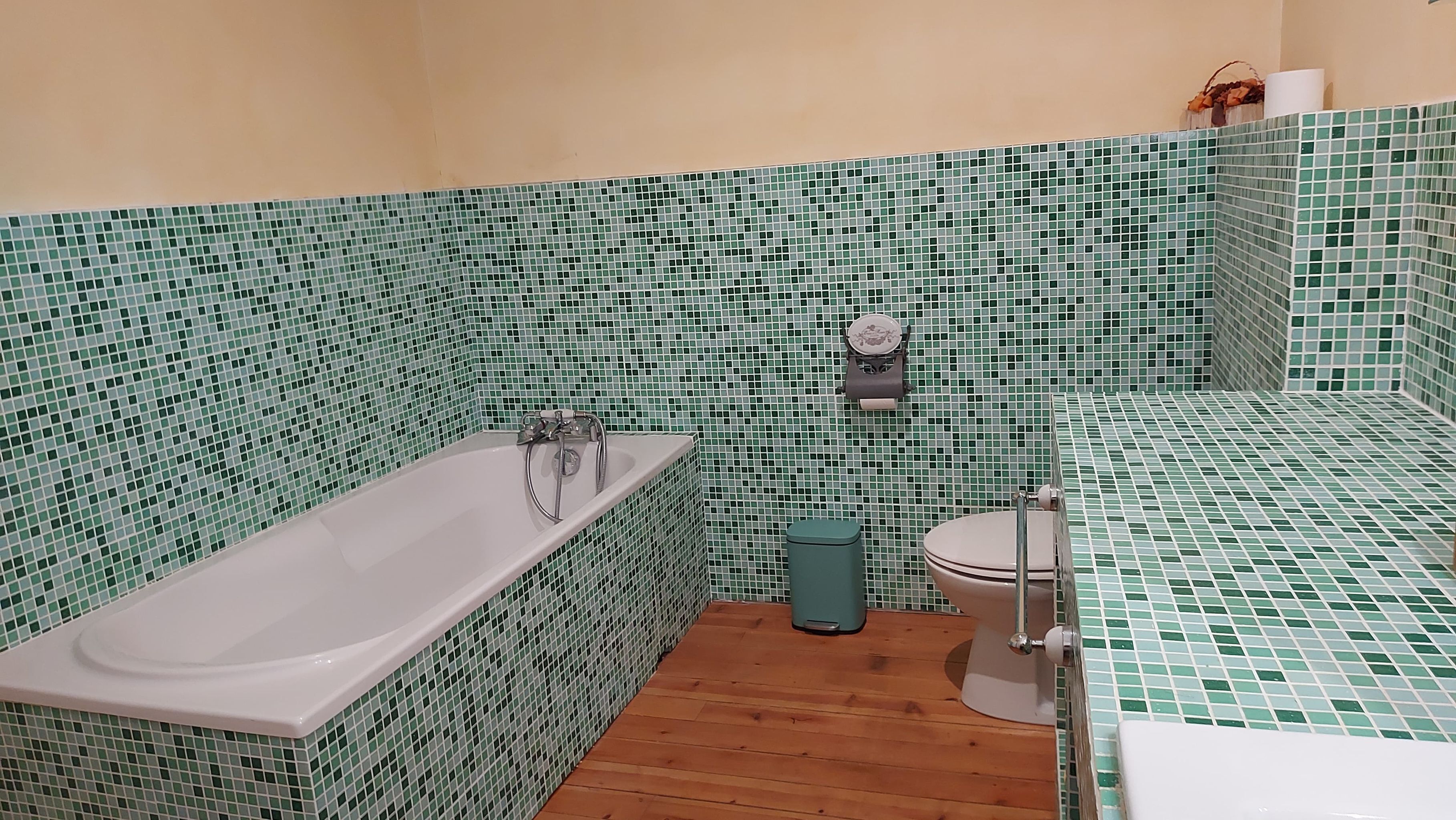 Une salle de bain avec une baignoire, des toilettes et un lavabo, le tout entouré de murs recouverts de mosaïques vertes.