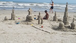 Una playa arenosa con varias esculturas de arena, incluyendo una torre grande y otras estructuras más pequeñas.