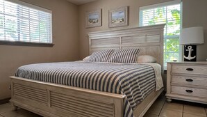 Un dormitorio con cama, mesita de noche y dos ventanas con persianas.