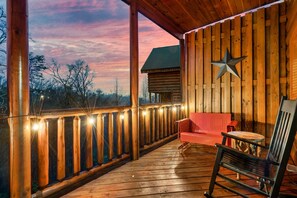 A wooden deck with a red bench and a star decoration, overlooking a forested area. - HUGE 86" THEATER w/ Stadium Seating, Resort Pool, Hot Tub, Pool Table, Views (Sevierville)
