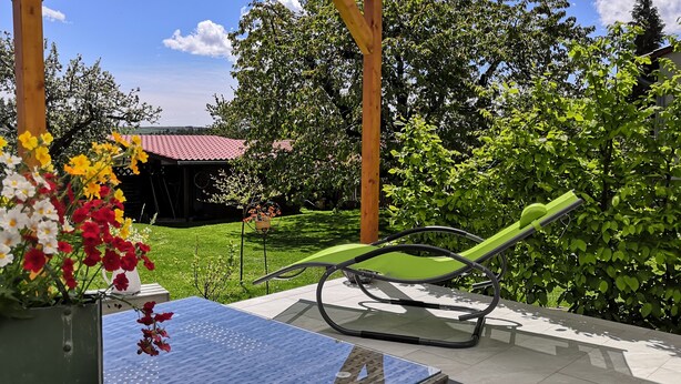 Eine Terrasse mit einem grünen Stuhl, einem Tisch und einem Blumentopf mit Blumen.