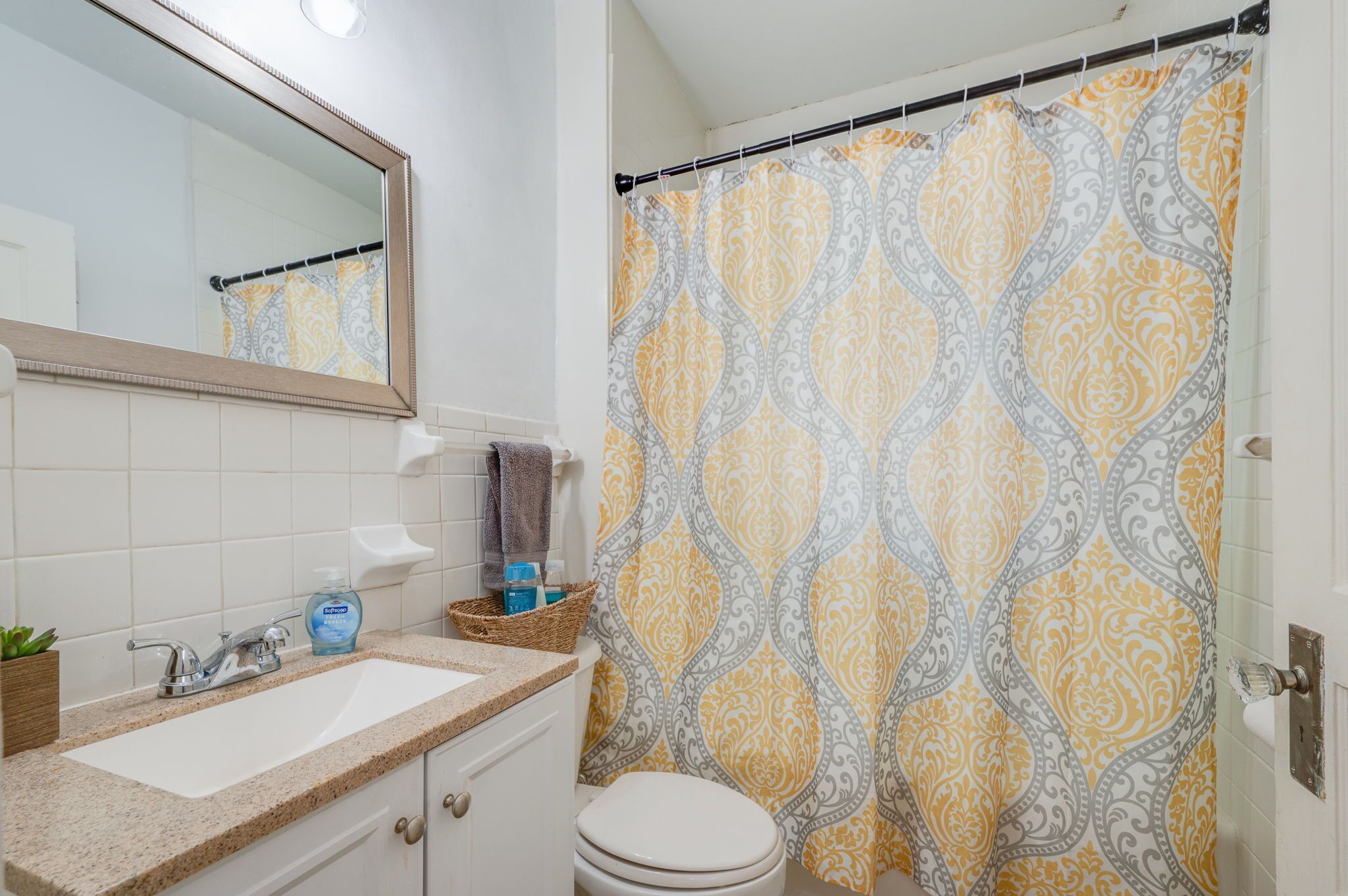 A bathroom with a sink, mirror, toilet, and shower curtain.