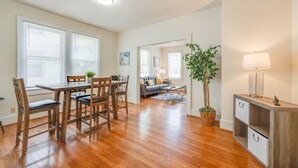 A spacious living area with a wooden dining table, chairs, a sofa, a lamp, and a potted plant.