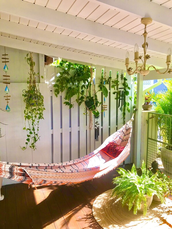 A hammock suspended between white slats, with hanging plants and a chandelier.