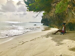 A person sitting on a sandy beach with a cliff and ocean in the background.