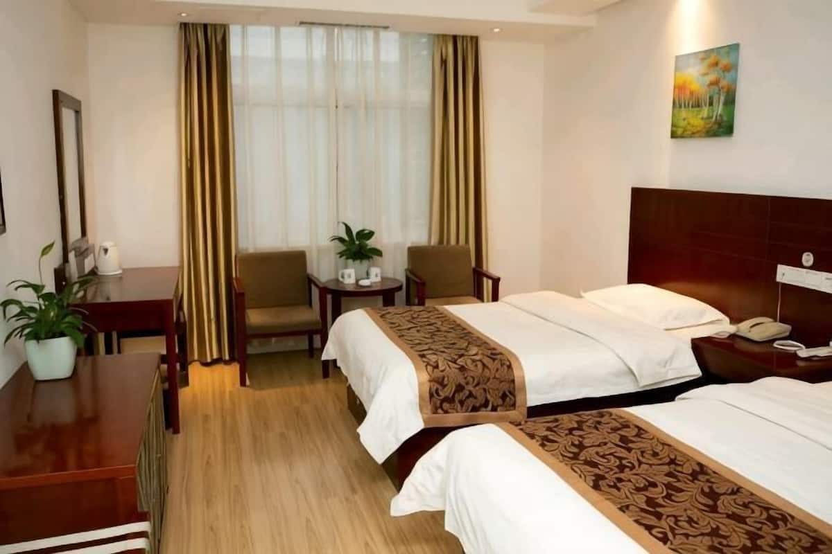 Ein Hotelzimmer mit zwei Betten, einem Schreibtisch, Stühlen, einem kleinen Tisch mit Pflanze und einem Gemälde an der Wand.
