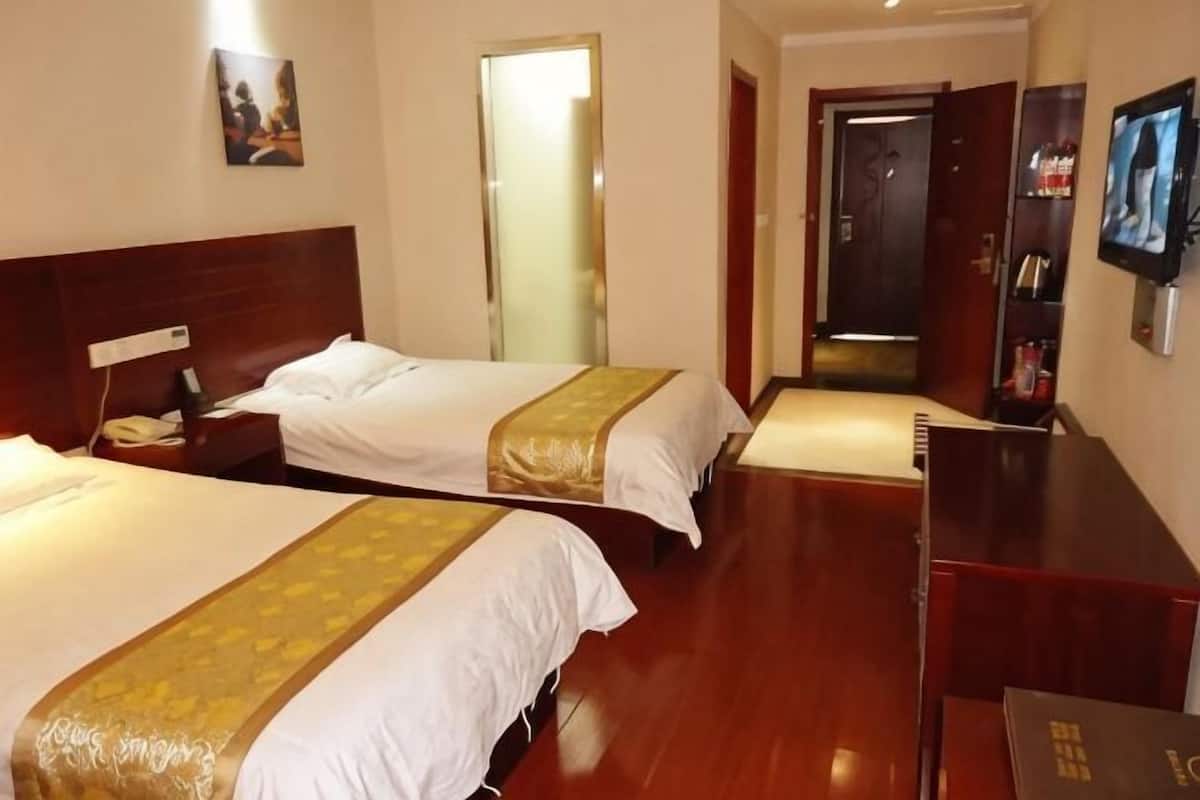 Ein Hotelzimmer mit zwei Betten, Holzboden, Fernseher und Spiegel.