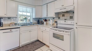 Een keuken met witte kastjes, een vaatwasser, een fornuis en een raam met uitzicht.