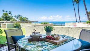 A patio with a table set for a meal, overlooking a beach and ocean. - Remodeled Condo Across Ocean w Pool AC-Shores of Maui 109 (Kihei)