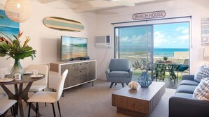 A beach house interior with a large window offering a view of the beach, a ceiling fan, and a dining area with a table and chairs. - Remodeled Condo Across Ocean w Pool AC-Shores of Maui 109 (Kihei)