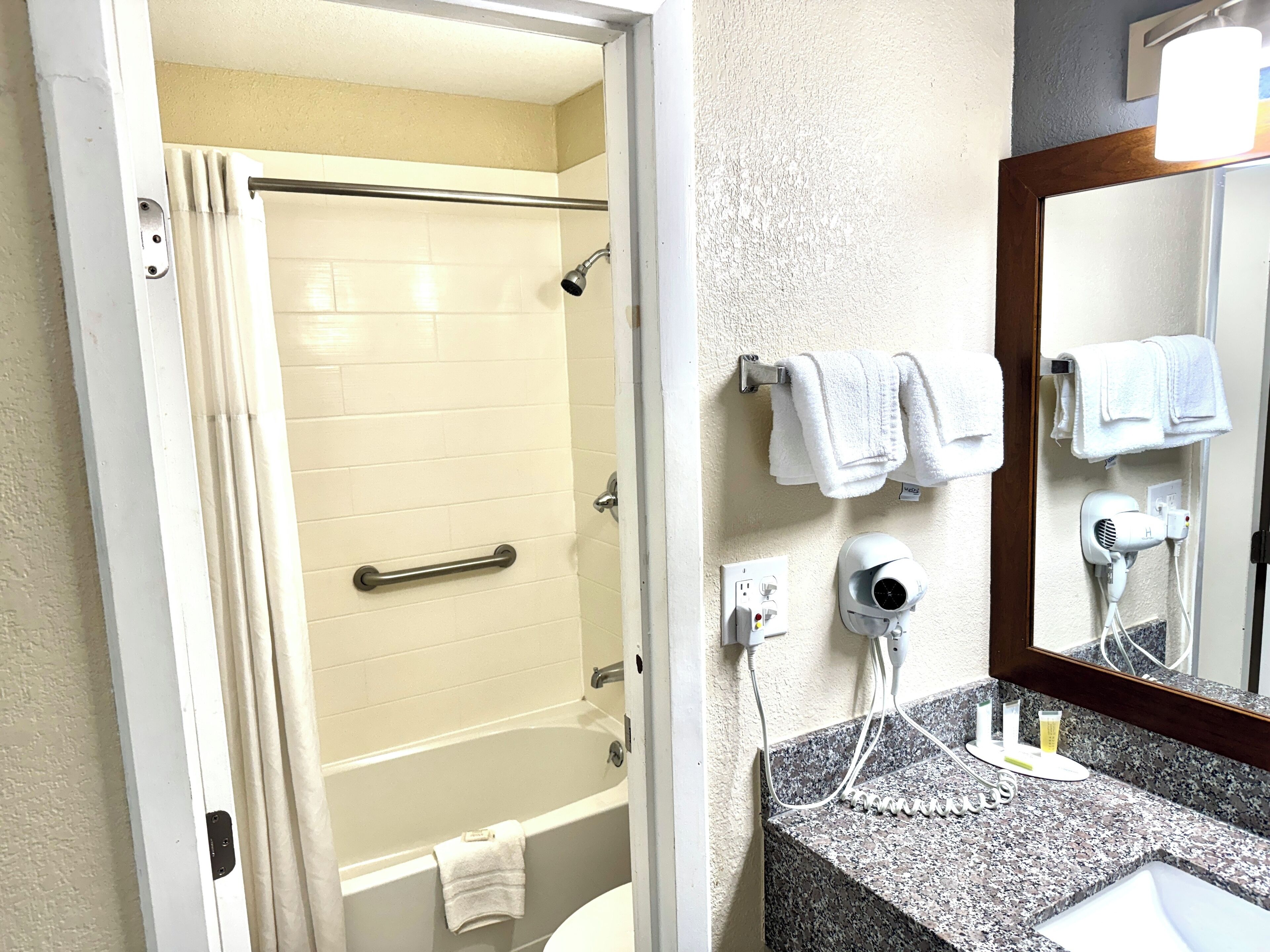 A bathroom with a shower, a toilet, a sink with a mirror, and a hairdryer on the wall.