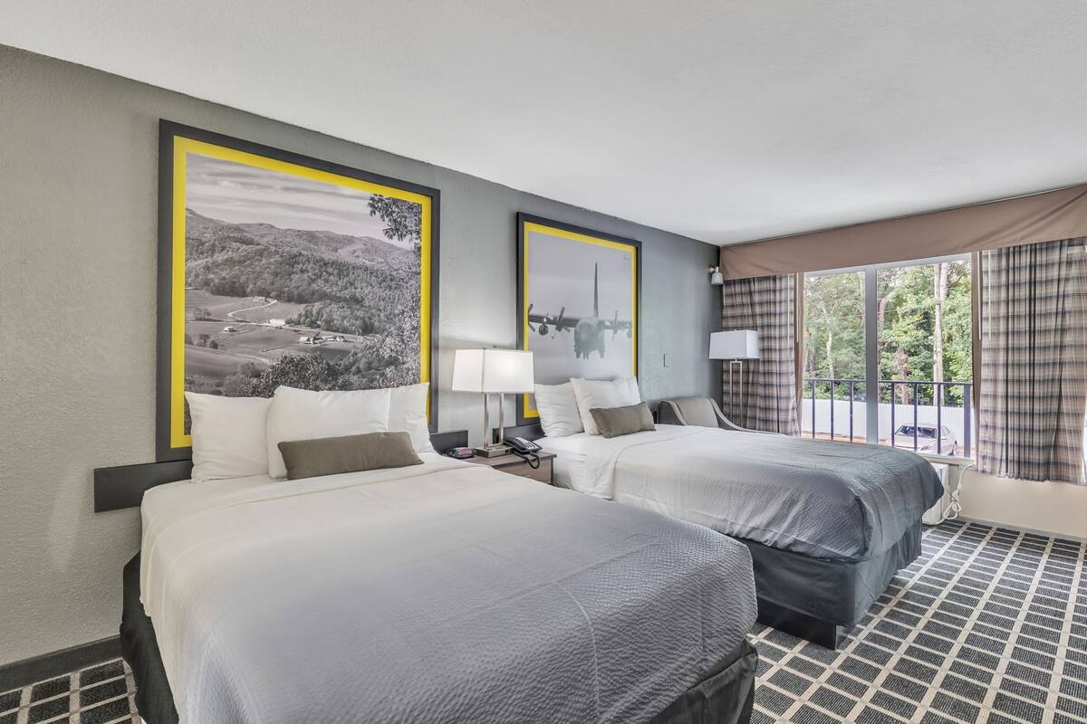 A hotel room with two beds, a large window with curtains, and two framed pictures on the wall.