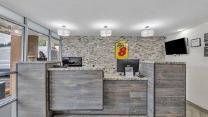 A reception area with a stone mosaic wall, a Super 8 sign, a flat-screen TV, and a wooden reception desk. - Super 8 by Wyndham Morganton (Morganton)