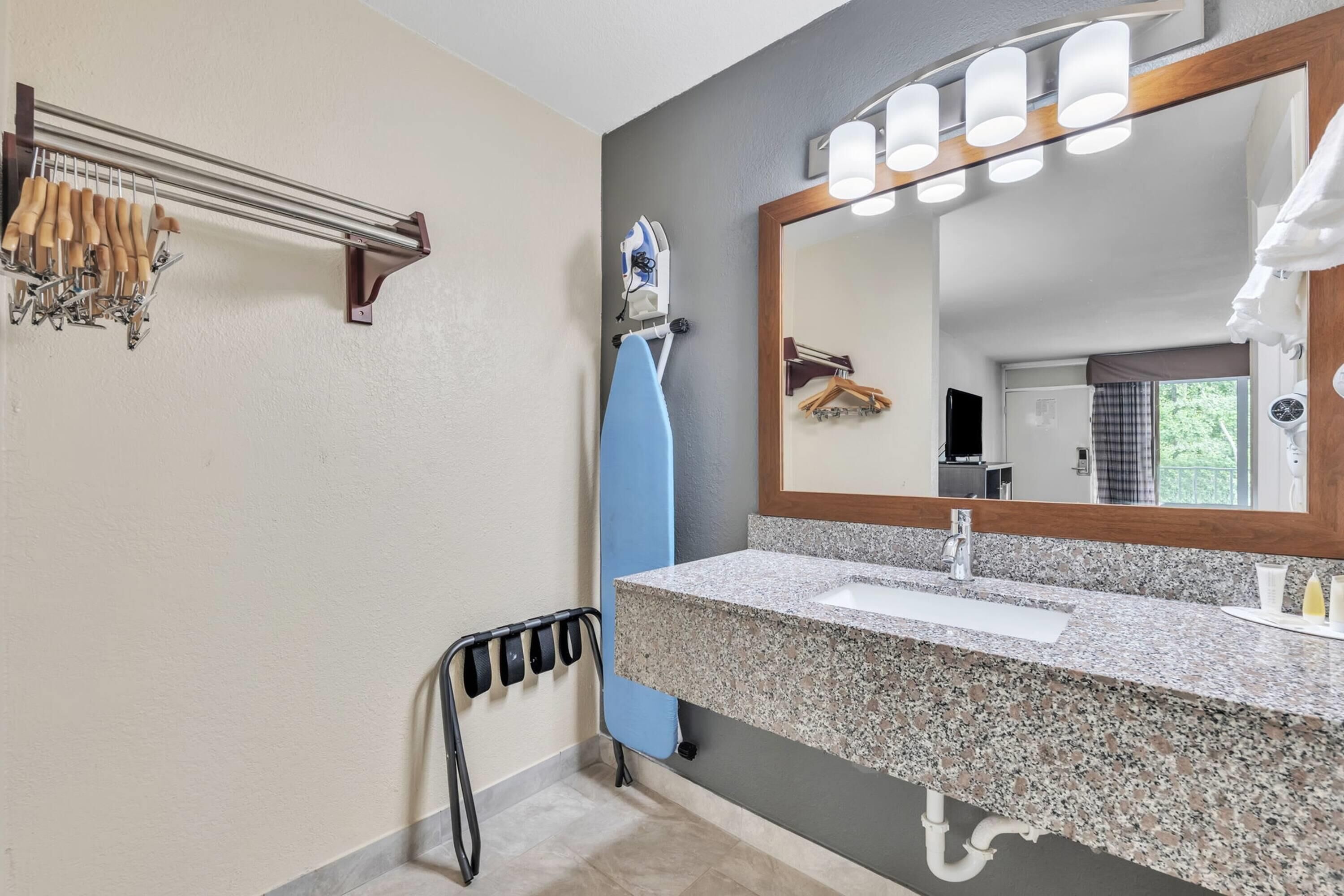 Un baño con lavamanos de encimera de granito, un espejo grande con luces, un perchero y un cesto de ducha azul.