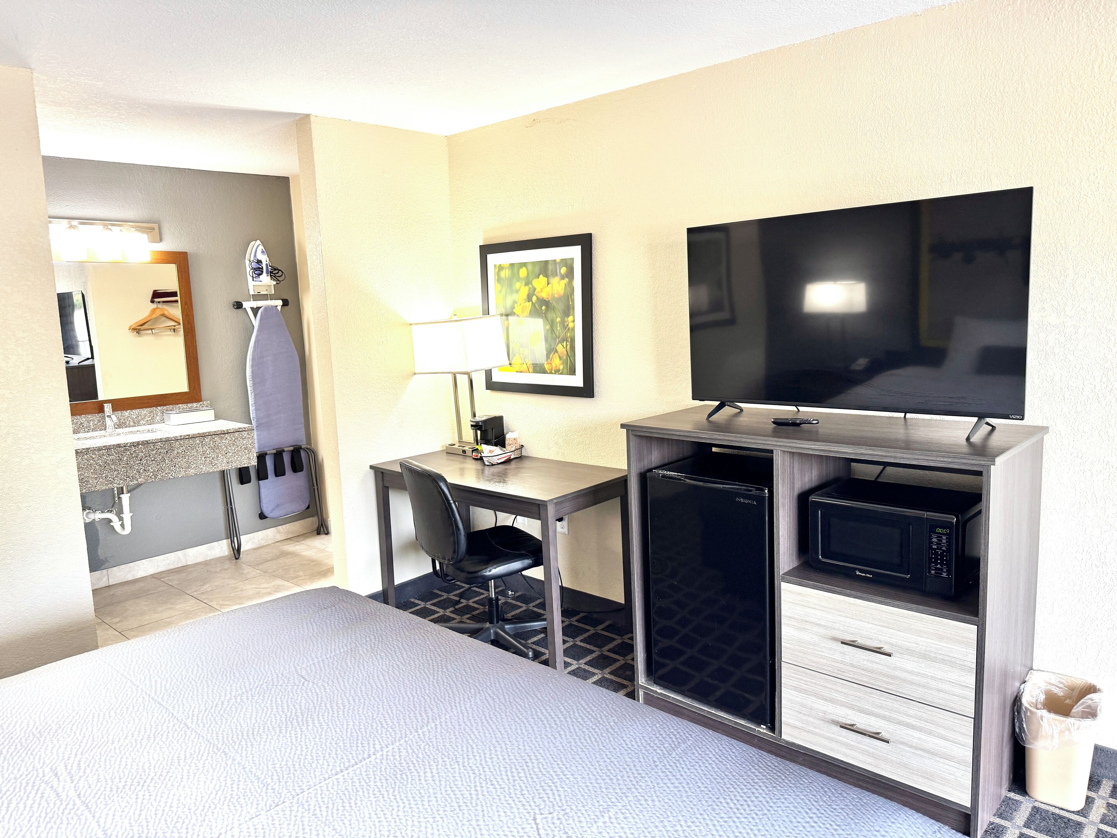 A hotel room with a desk, chair, television, microwave, and a small kitchenette.