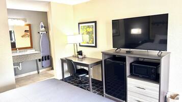 A hotel room with a desk, chair, television, microwave, and a small kitchenette.