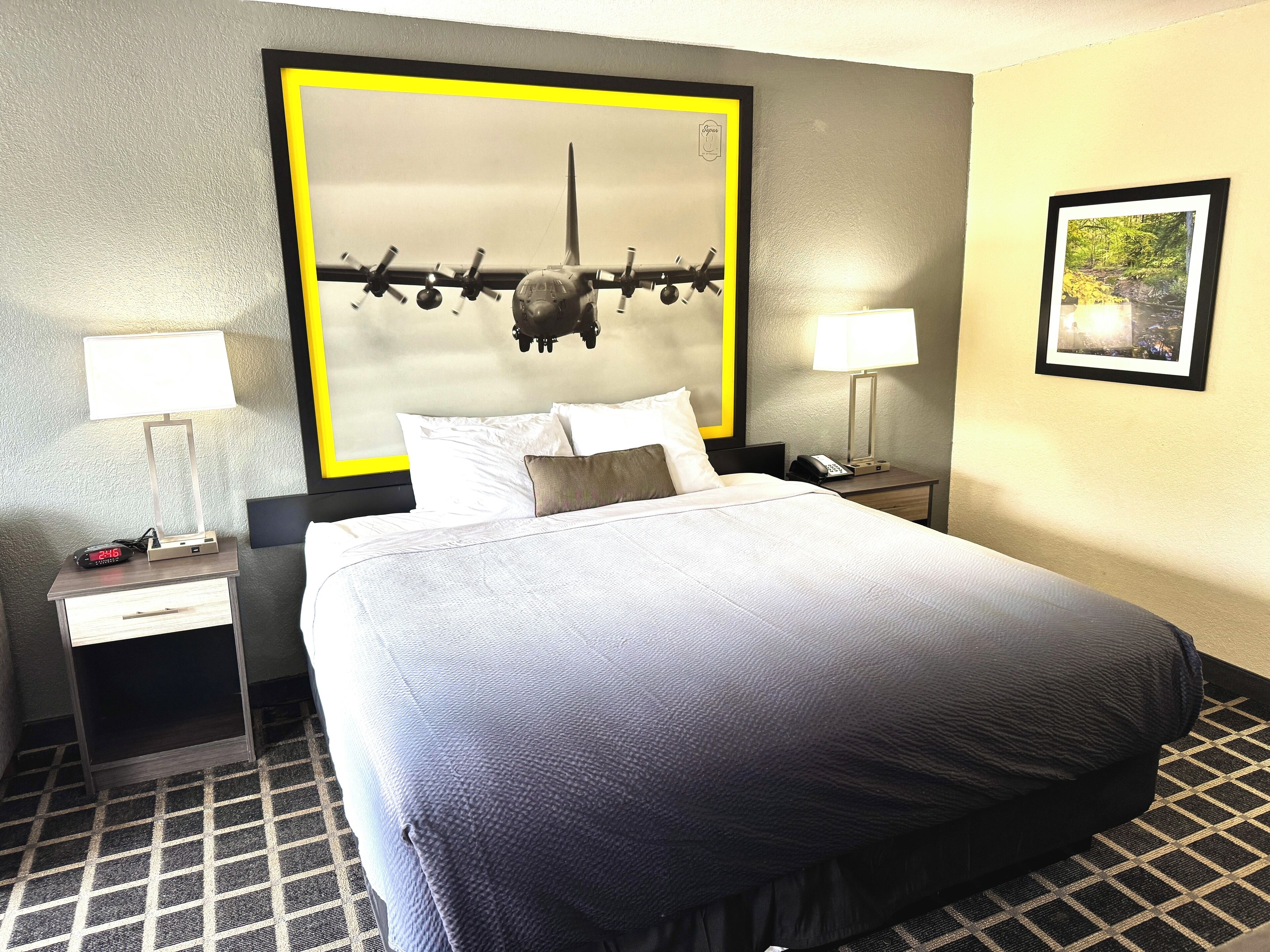A hotel room with a large bed, two bedside tables with lamps, a clock, and a framed picture on the wall.