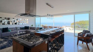 Une cuisine moderne dotée d’un îlot central, de tabourets de bar et d’un coin repas offrant une vue sur la mer.