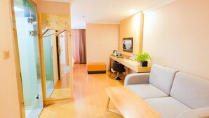 A modern hotel room with a wooden floor, a sofa, a desk with a computer, a small table, and a glass door leading to a shower area. - Greenhouse Hotel, Tongji Hospital, Guangxin Road, Shanghai (Shanghai)