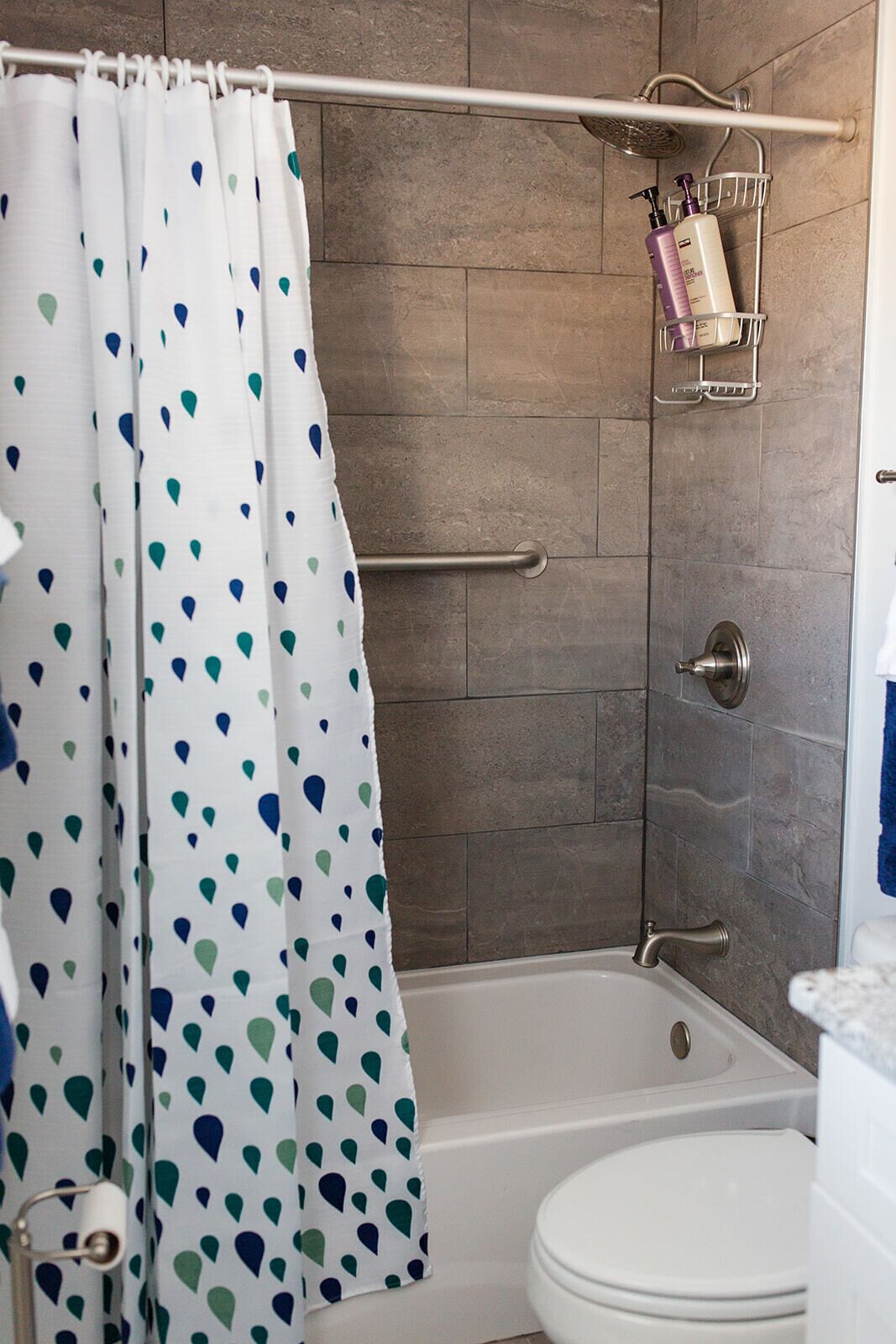A bathroom with a shower curtain, a bathtub, a toilet, and a towel rack with toiletries.