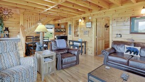 A wooden cabin interior with a dining area, leather sofas, and a ceiling fan.