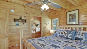 A wooden cabin bedroom with a bed, a ceiling fan, a framed picture, and a wooden door.