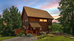 A log cabin with a porch, a picnic table, and a stone fireplace.