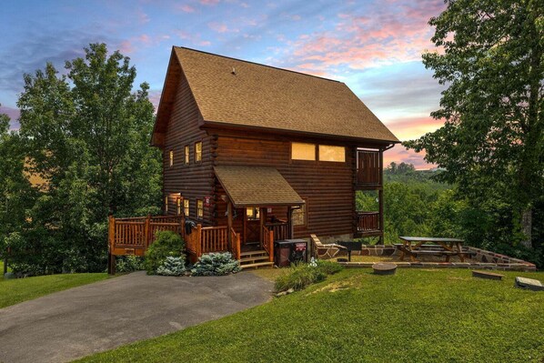A log cabin with a porch, a picnic table, and a stone fireplace.