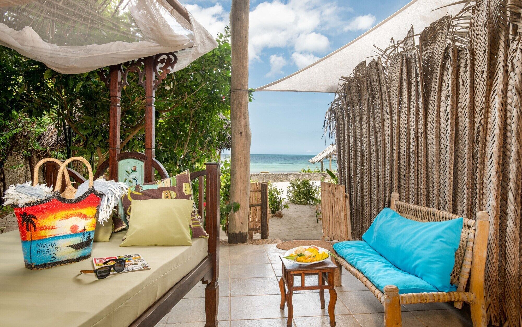 Eine Terrasse direkt am Strand mit einer Rattan-Couch, einem Tisch mit Essen und einer bunten Tasche.
