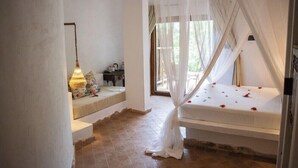 A bedroom with a canopy bed, a bedside table, a lamp, and a view of the outdoors. - Mvuvi Boutique Resort (Kiwengwa)