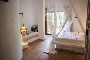 Une chambre à coucher avec un lit à baldaquin, une table de chevet, une lampe et une vue sur l’extérieur.