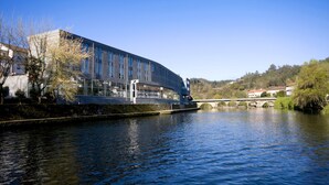 Un bâtiment moderne doté de grandes fenêtres donnant sur une rivière, un pont et un paysage vallonné.