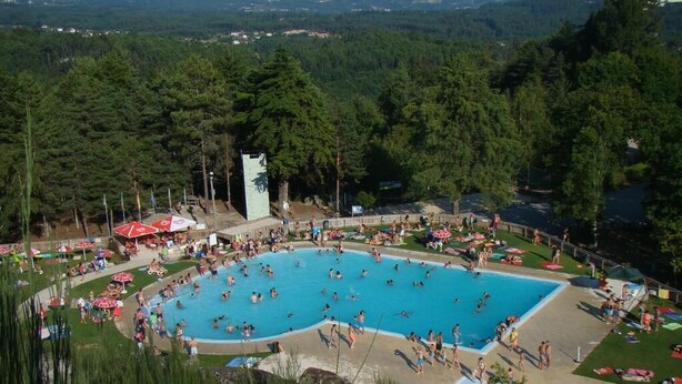 Une grande piscine extérieure entourée d’une végétation luxuriante et agrémentée d’une petite tour.