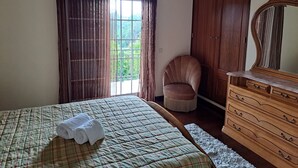 Une chambre à coucher avec un lit, une chaise, une commode et une fenêtre avec des rideaux.