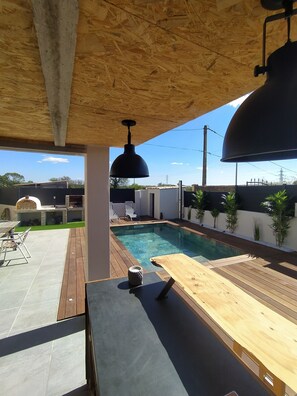 An outdoor pool area with a wooden deck, a barbecue grill, and a seating area with chairs and a table. - Villa with swimming pool located in a condominium near Béziers (Béziers)