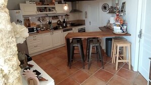 A kitchen with a central island, white cabinets, and a stone wall. - Villa with swimming pool located in a condominium near Béziers (Béziers)
