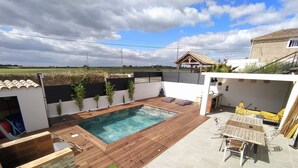 A backyard with a swimming pool, a wooden deck, a patio with a table and chairs, and a small garden area. - Villa with swimming pool located in a condominium near Béziers (Béziers)
