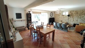 A spacious living area with a wooden dining table, chairs, and a stone wall. - Villa with swimming pool located in a condominium near Béziers (Béziers)
