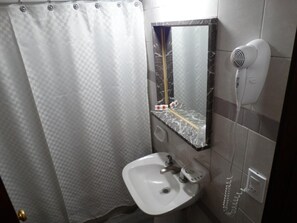Een badkamer met een wit wastafelmeubel, een spiegel met een marmeren lijst, een douchegordijn en een haardroger aan de muur.