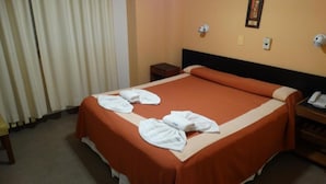 A hotel room with a neatly made bed, a bedside table with a phone, and a wall-mounted light.
