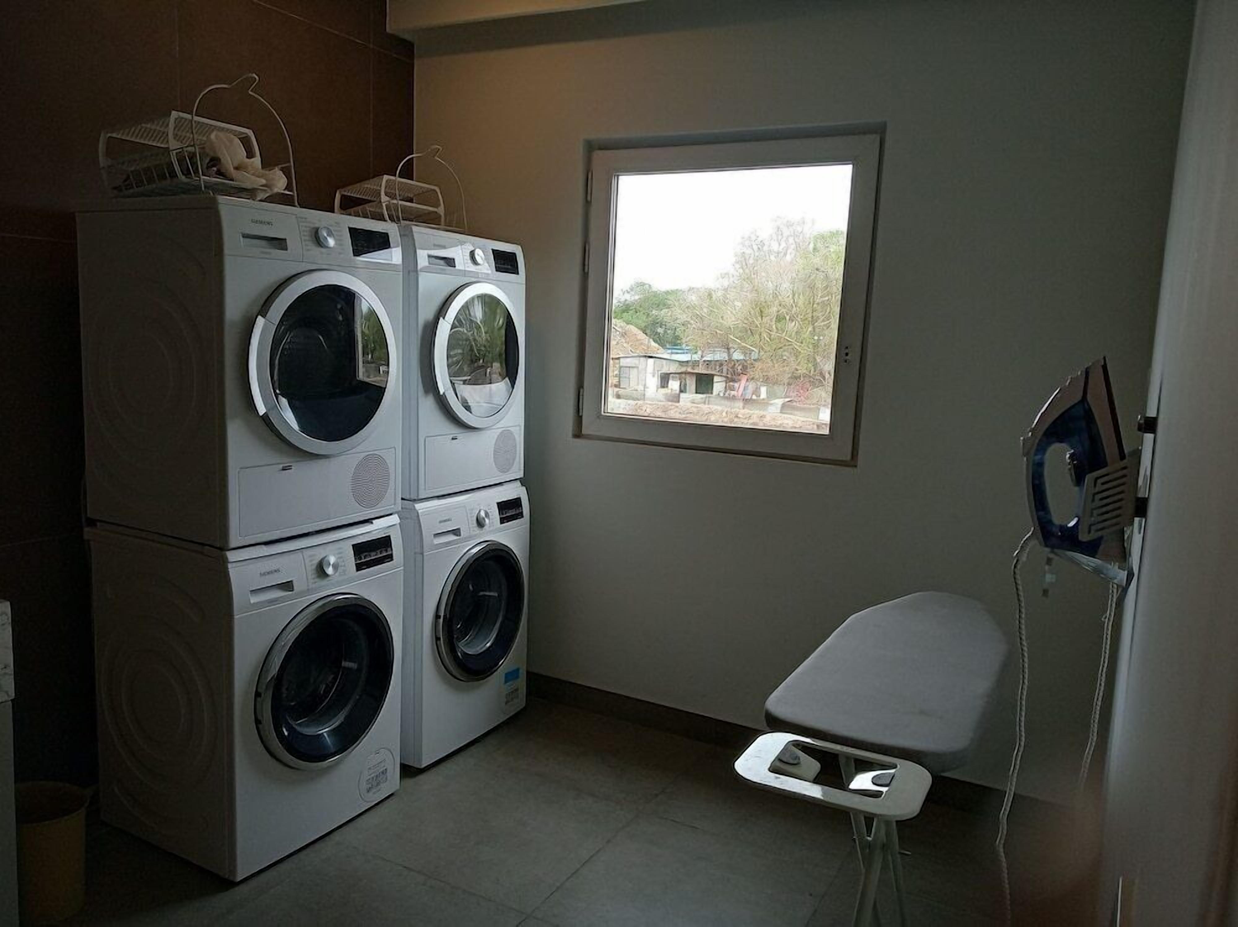 A laundry room with stacked washers and dryers, a window with a view, and a small ironing station.