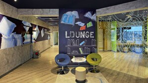 A modern lounge area with a large wall displaying 'Lounge' and images of books, a small table with magazines, and two colorful chairs. - Holiday Inn Express Pune Pimpri (Pune)