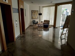 Un vestíbulo espacioso con un suelo de mármol pulido, una zona de estar con una mesa redonda y un gran cuadro abstracto en la pared.