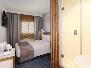 A hotel room with a bed, a desk with a coffee maker, a TV, and a window with blinds. - Holiday Inn Express Pune Pimpri (Pune)