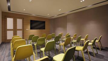 A conference room with rows of chairs, a flat-screen TV on the wall, and a carpeted floor.