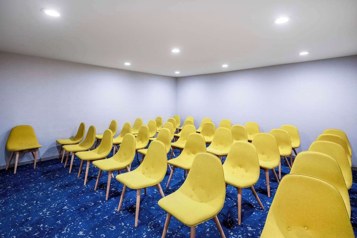 A conference room with rows of yellow chairs and a blue carpeted floor.